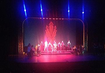 A group of people performing on a stage with colorful lighting.