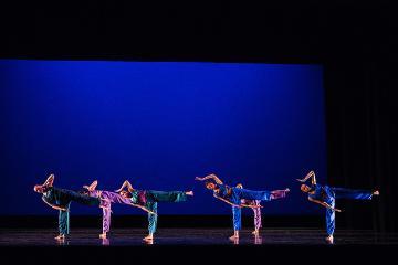 Dancers performing on stage with a blue background.