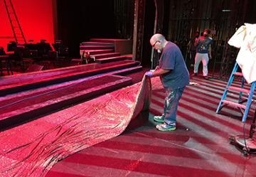 Person working on theater stage set with red carpeting.