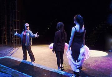 Three performers on stage with colorful lighting and dramatic poses.