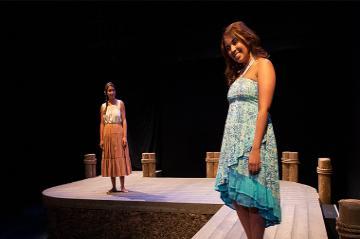 Two women standing on a stage, one wearing a blue dress.