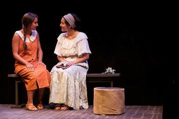 Two women in costume sitting on stage in a dark setting.