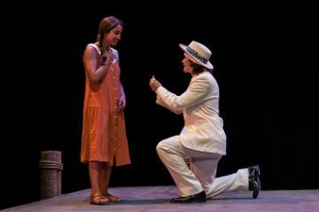 Person in suit kneeling before a person in dress on stage.