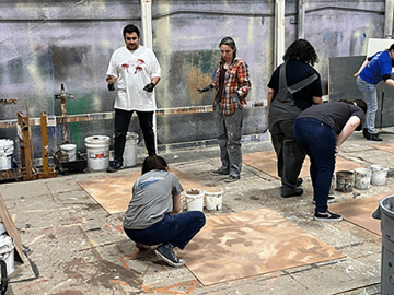 3 female and 1 male student with a female instructor learning to paint wall textures for stage scenery