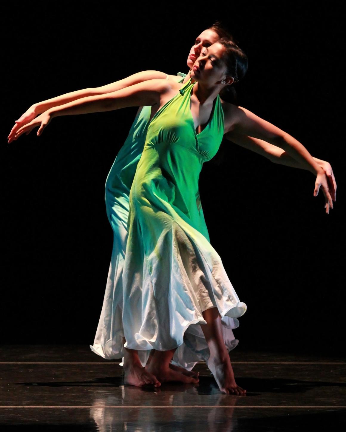 A dancer performs a graceful move in green and white attire.