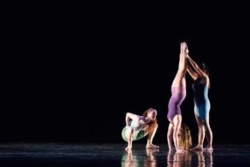 Three dancers performing modern dance on a dark stage.