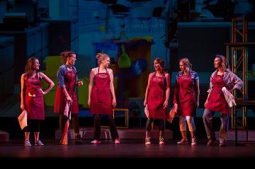 Five people on stage in red outfits performing under dramatic lighting.