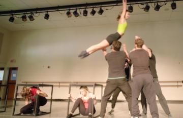 Dance student jumping from a table to be caught by 2 other dancers in a studio