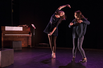 Two people dancing on a stage with dim lighting.