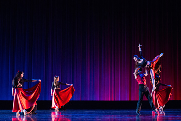 Dancers in red performing against a purple and blue lit backdrop.