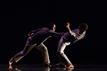 Two dancers dynamically performing on stage against a black background.