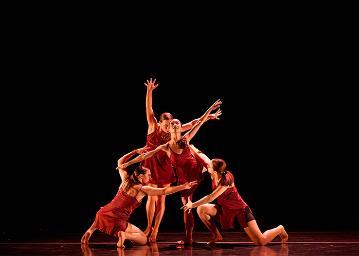 In a clump, 2 female dancers in red strappy dresses standing reaching to the audience and 2 female dancers in red strappy dresses kneeling with arms held out to each other