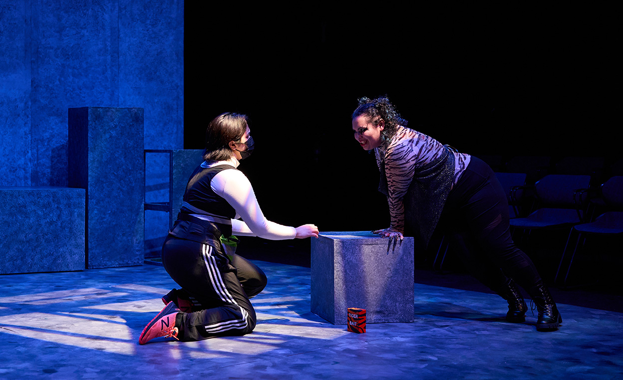 A female runner in a white top and black jogging pants kneeling by a platform on which a fictional tiger character leans