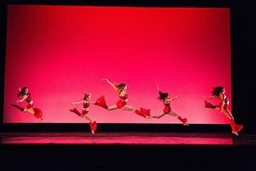 Dancers performing on a stage with a red background.