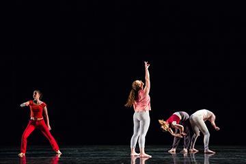 Four performers dancing on a dark stage in various poses.