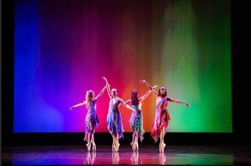 Five dancers perform on stage with a multicolored background.