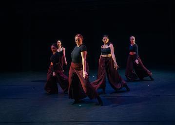 5 female dancers in black tops and maroon flowing pants in a vee formation