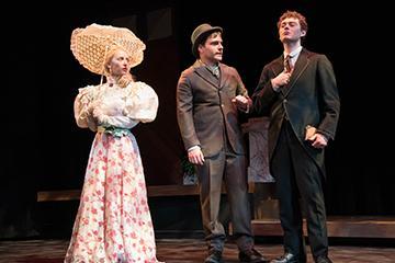 Three actors performing on stage in period costumes.