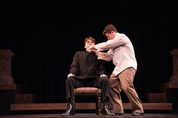 A doctor examining a man seated on a chair on stage.