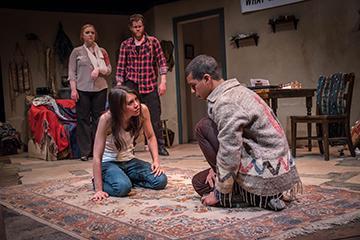 Four people in a staged theatrical scene with one kneeling and one seated.