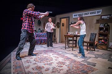 Two actors stage a confrontation in a rustic room.