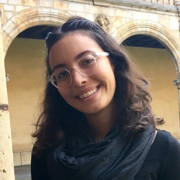 A person smiling in a historical courtyard with arches.