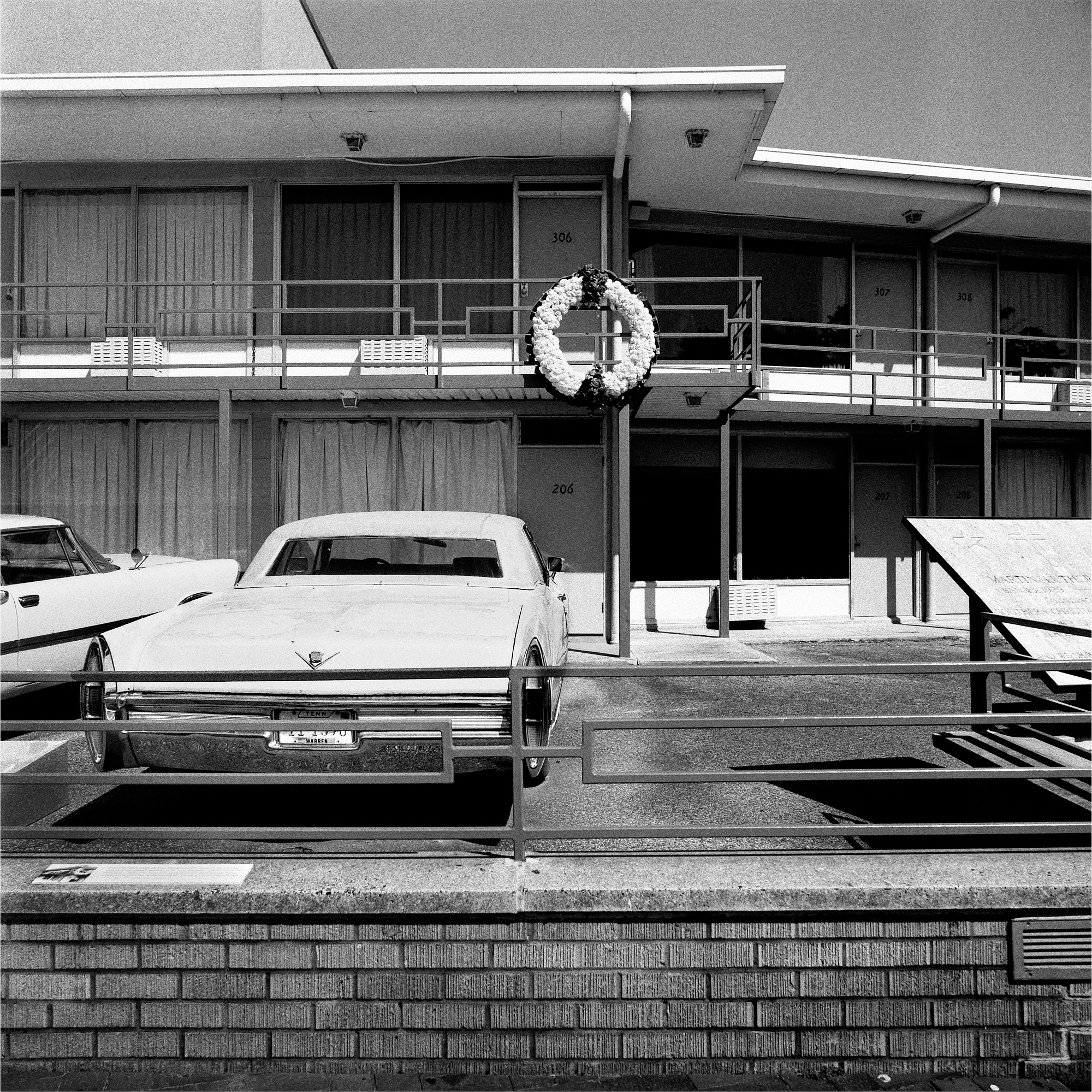 Black and white photograph of cars in parking lot in front of room at Lorraine Hotel with memorial wreath hanging in front of room 306