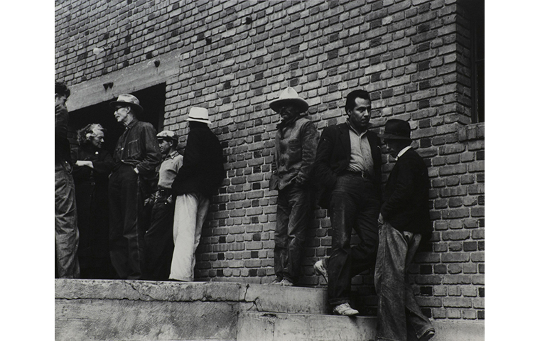 Black and white photograph of eight laborers on strike standing outside of brick building.