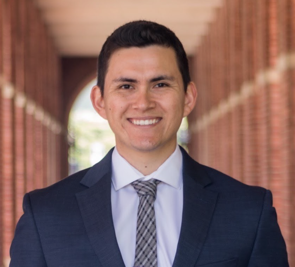 A person in a suit smiling with a brick archway background.