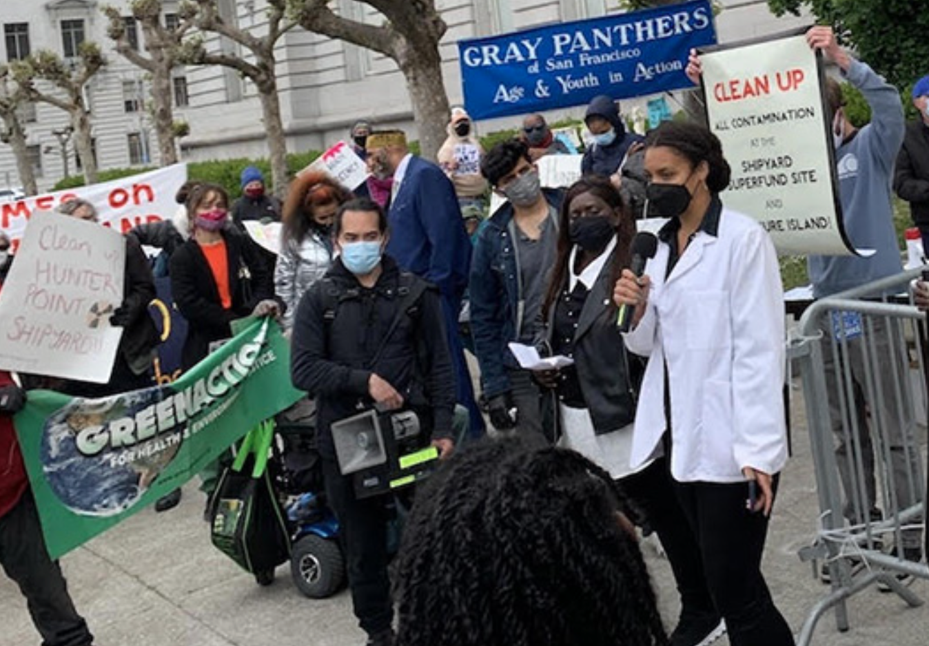 Reporter standing with mike and others participating in a procession