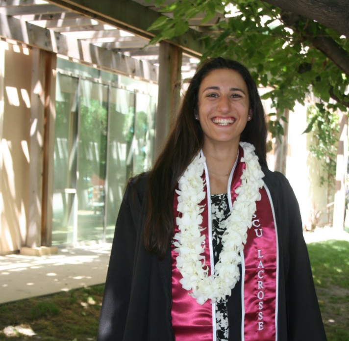 A person smiling, wearing a lei and graduation attire.