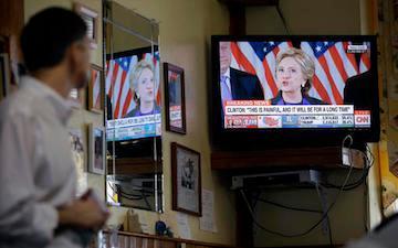Person watching Hillary Clinton concession speech on TV with American flags in the background.