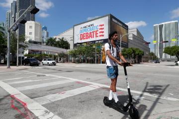 A person rides a scooter near a Democratic presidential debate banner.