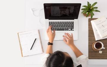 person sitting at table with open laptop, notebook and pen