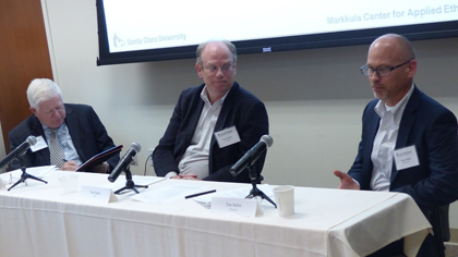 Three men sitting at a panel table with microphones, discussing taxes.