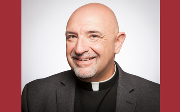 A smiling person wearing a clerical collar and suit jacket.