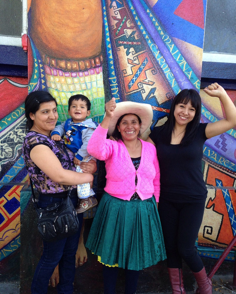 Three women and a child in front of a colorful mural.