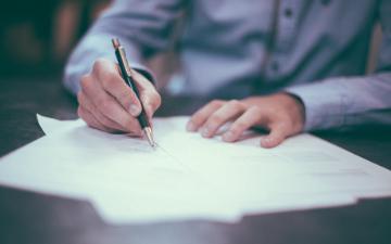 A person writing on papers. Photo credit: Scott Graham/Unsplash 
