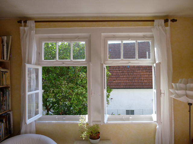 A room with an open window, white curtains, and outdoor view.