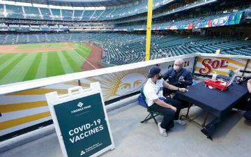 People receiving vaccines at a baseball stadium with a sign reading 