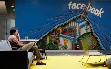 A person sitting in a room with a Facebook-themed wall mural.