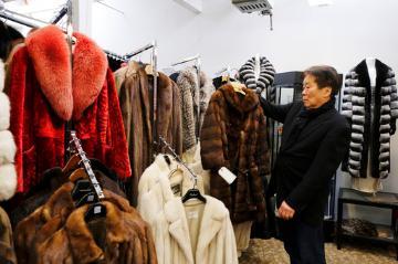 Person browsing fur coats in a store labeled 