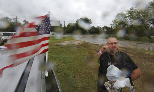 A person carrying supplies stands next to a car with a U.S. flag.