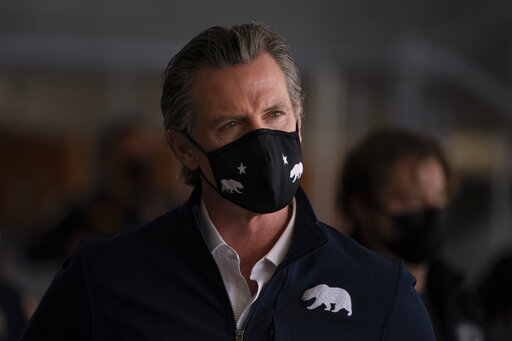 A man wearing a black face mask and navy jacket with a bear emblem.