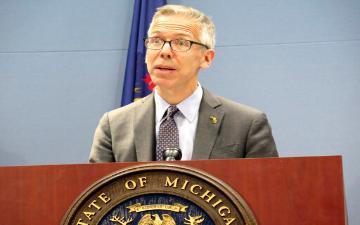 A man speaking at a podium with an official seal.