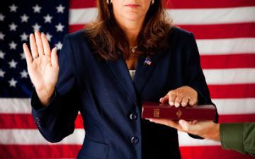 Person taking an oath with hand raised and holding a book.