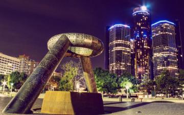 Monument of a fist in front of lit skyscrapers in Detroit at night.