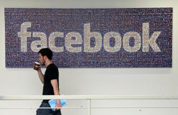 Man walking past a wall with a large Facebook logo.