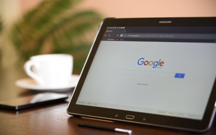 Tablet displaying Google search engine on screen, next to a cup and laptop.