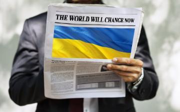 A person holding a newspaper with a large Ukrainian flag on the front page.